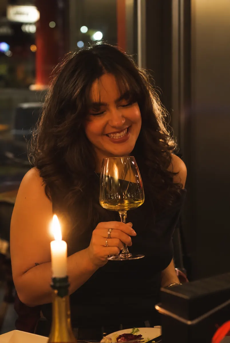 A guest smiling over a glass of white wine by candlelight