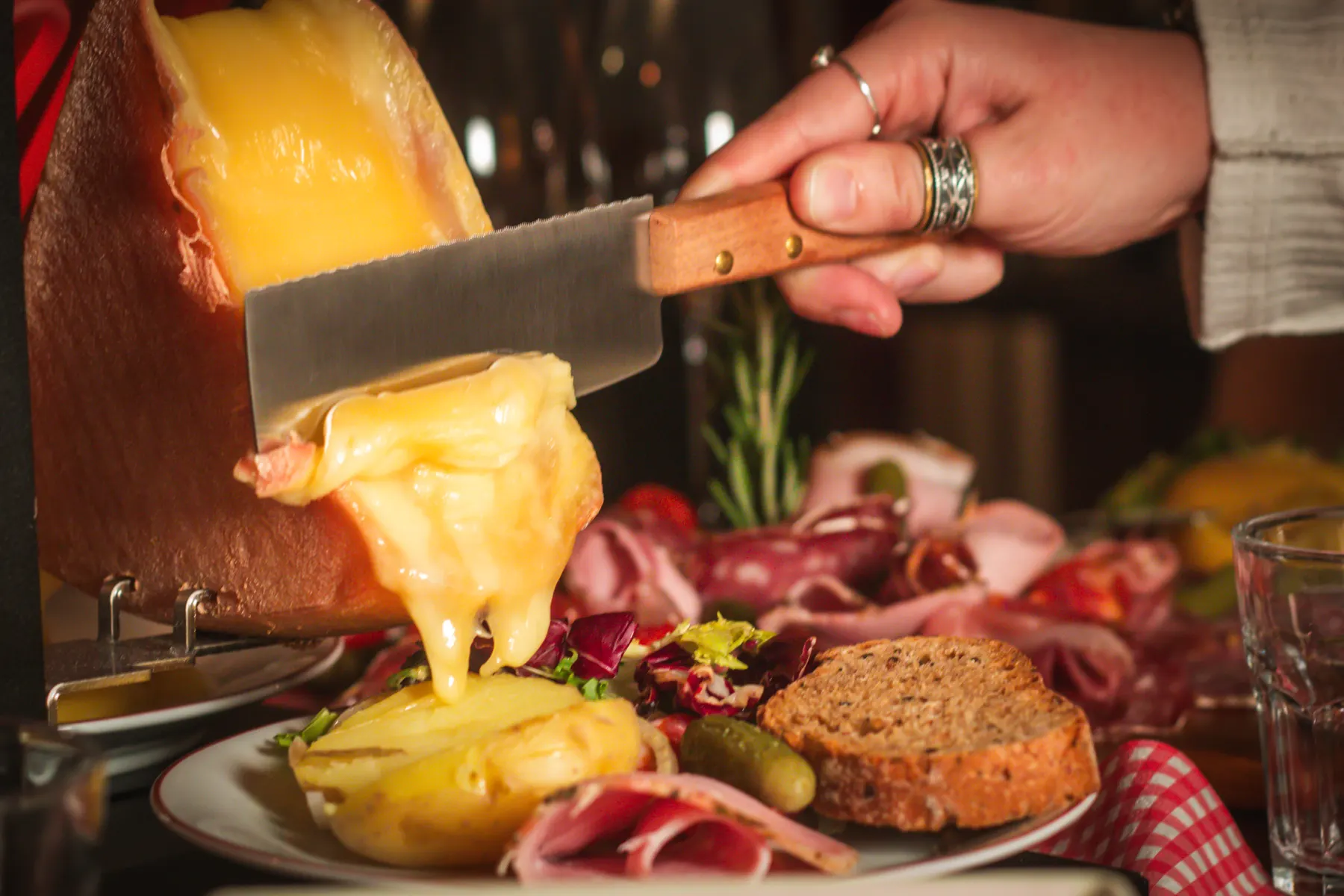Melted raclette being scraped from the wheel onto potatoes, bread and charcuterie
