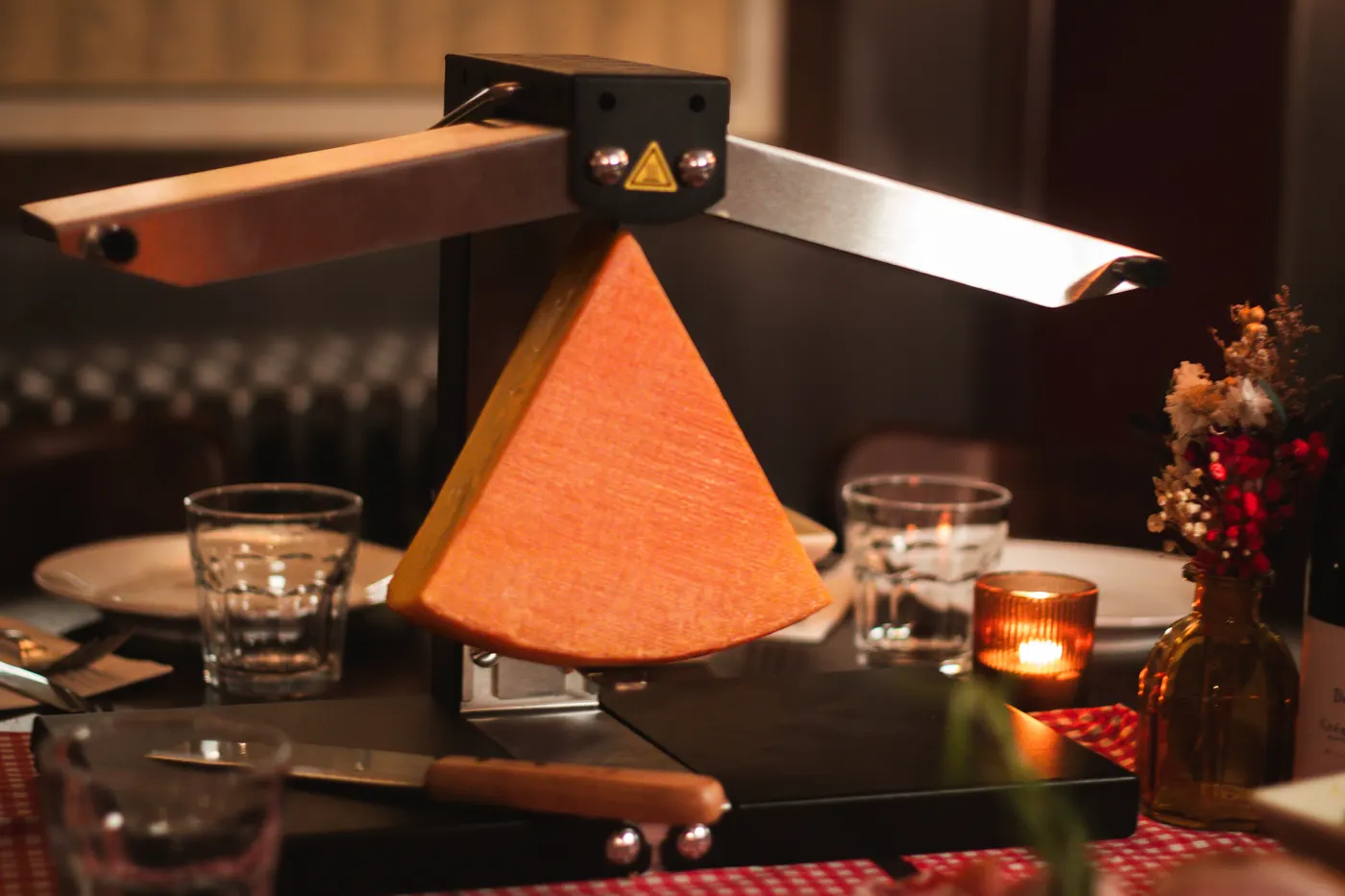 A quarter-wheel of raclette under its heating bar, with a charcuterie board, salad and wine
