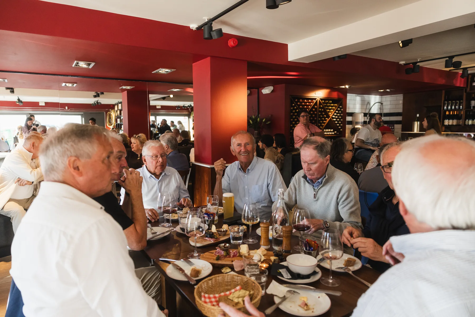 Guests at Chez Bernard passing a bottle of wine across a table of cheese, charcuterie and glasses